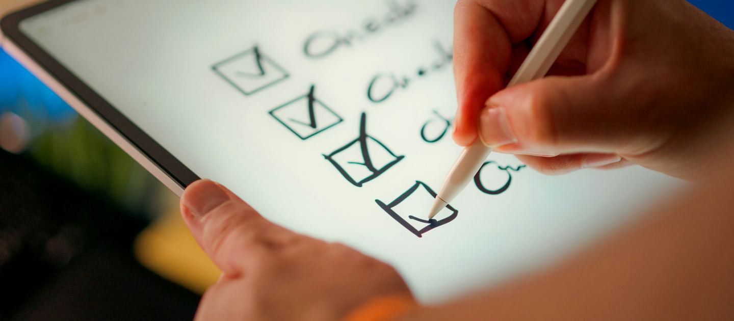 A hand ticking items off a checklist on a tablet.