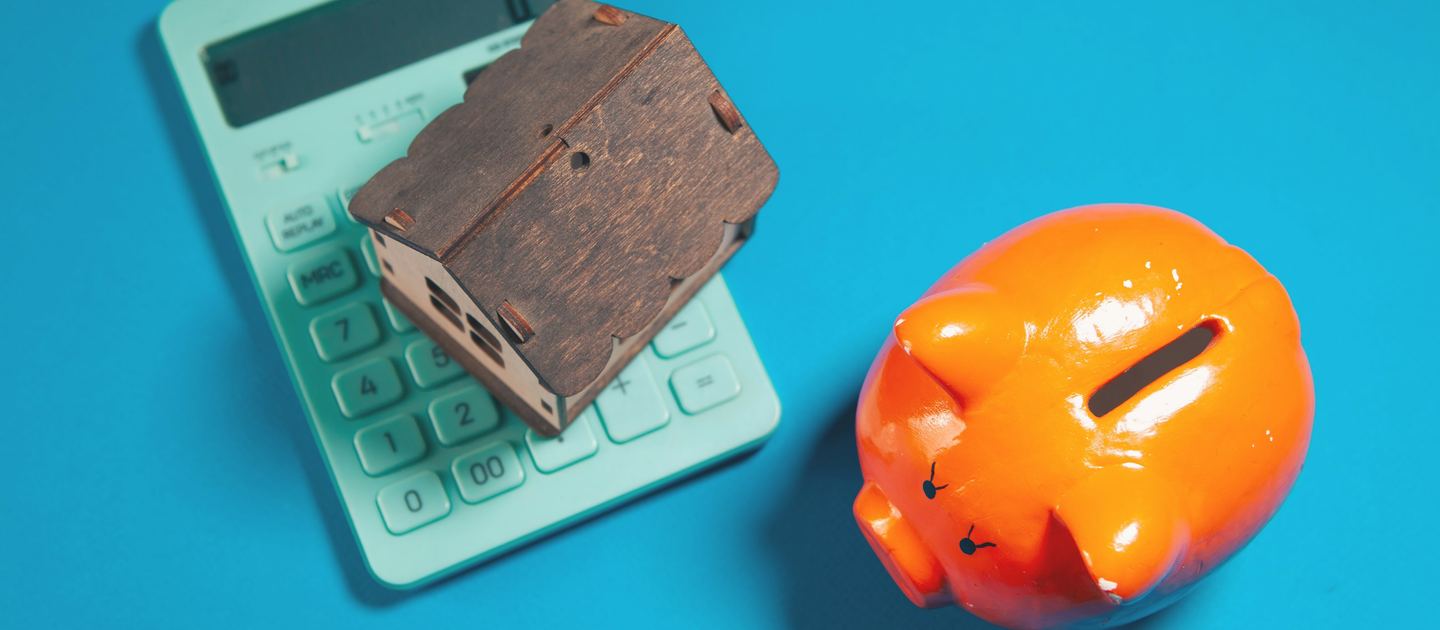 A calculator, a model house and a piggy bank on a blue background.